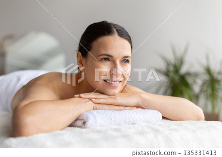 Smiling woman resting during spa treatment, lying on massage bed Smiling woman resting during spa treatment, lying on massage bed 135331413
