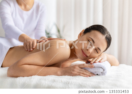 Relaxed woman enjoying back massage at spa, eyes closed and smiling softly 135331453