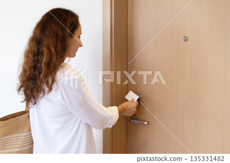 Adult woman using key card to unlock hotel room door after arrival 135331482