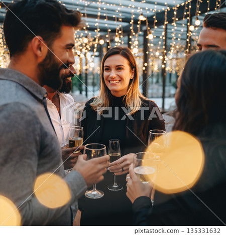 Friends gather to celebrate with drinks at a lively evening party under string lights 135331632