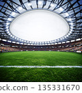 Wide-angle view of a large stadium with green field and crowds during a daytime sports event 135331670