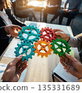 Close up of hands holding colorful gears during a collaborative work session in an office setting with people in the background 135331689