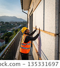Construction worker installs panels on building exterior during evening hours with mountains in the background 135331697