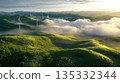 Wind farm on a green hillside at sunrise with fog and turbines rising above creating dramatic lighting 135332344