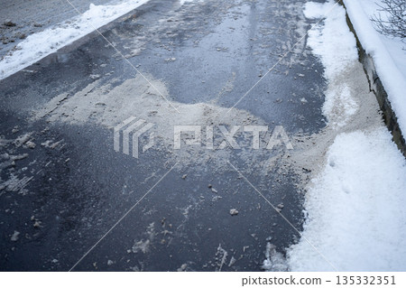Deicing chemicals on snowy street in winter. Slippery road sprinkled with technical salt 135332351