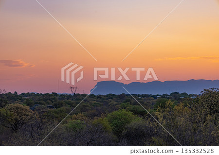 Orange and purple sunset sky over silhouetted mountains and green bushland Orange and purple sunset sky over silhouetted mountains and green bushland 135332528