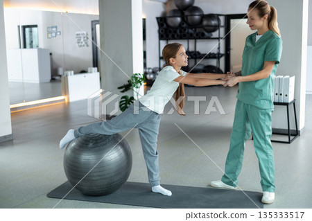 Pediatric physiotherapist helping child balance on therapy ball Pediatric physiotherapist helping child balance on therapy ball 135333517