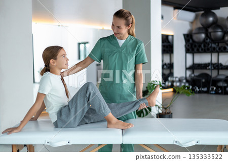 Physiotherapist assisting child with leg movement exercise Physiotherapist assisting child with leg movement exercise 135333522