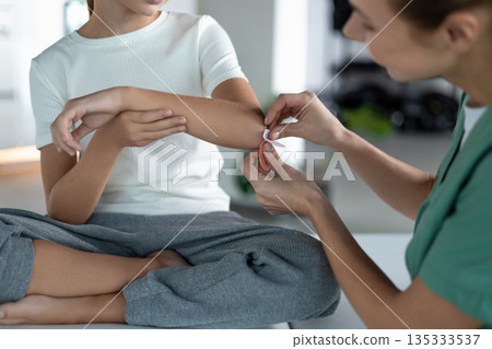 Nurse cleaning and covering minor injury on girl's arm Nurse cleaning and covering minor injury on girl's arm 135333537