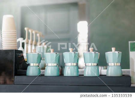 Close-up moka coffee pot placed on a black wooden table counter. moka pot coffee Beautiful colors, minimalist style, campsite morning picnic lifestyle, cooking hot drink in nature camping. 135333539