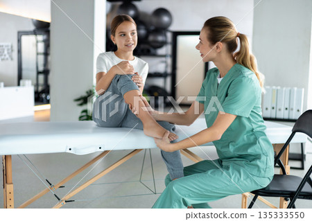 Physiotherapist helping young girl perform knee exercise 135333550