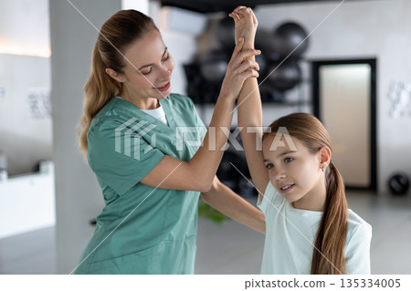 Woman therapist lifting little girl arm demonstrating range of motion Woman therapist lifting little girl arm demonstrating range of motion 135334005