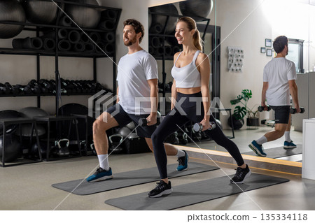 Young man and woman exercising with dumbbells and doing forward lunge 135334118