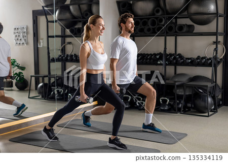 Young man and woman exercising with dumbbells and doing forward lunge Young man and woman exercising with dumbbells and doing forward lunge 135334119