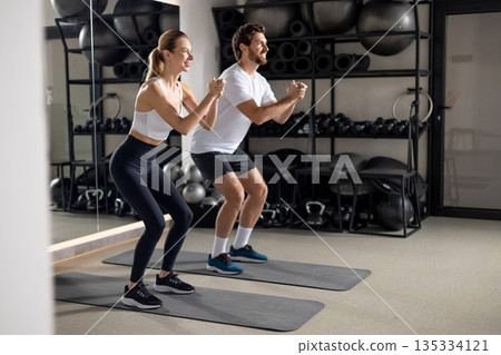 Two young people exercising in the gym in squatting position Two young people exercising in the gym in squatting position 135334121
