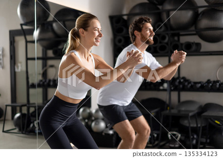 Two young people exercising in the gym in squatting position Two young people exercising in the gym in squatting position 135334123