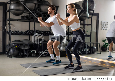 Two young people exercising in the gym in squatting position Two young people exercising in the gym in squatting position 135334124