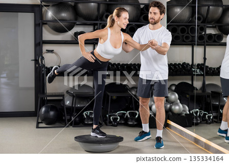 Male coach and a young woman having balance board workout and looking focused Male coach and a young woman having balance board workout and looking focused 135334164