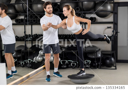 Male coach and a young woman having balance board workout and looking focused Male coach and a young woman having balance board workout and looking focused 135334165