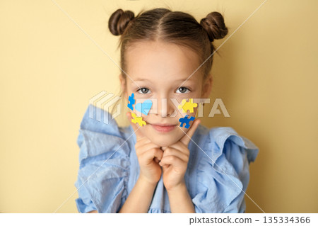 The child demonstrates the yellow and blue puzzle elements pasted on his cheeks as a sign of support for children with down syndrome. 135334366