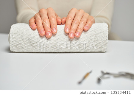 Woman hands with natural nails resting on a white towel, preparing for a manicure 135334411