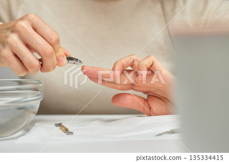 Woman's hands performing a home manicure, cutting cuticles with nippers for nail care 135334415