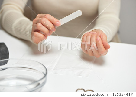 Woman filing fingernails during personal self-care beauty routine Woman filing fingernails during personal self-care beauty routine 135334417