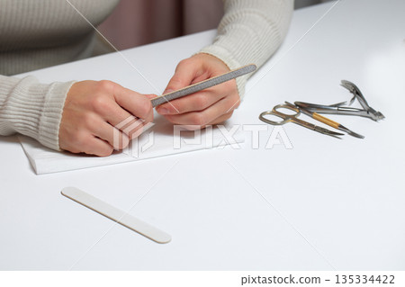 Woman performing a self-manicure using a nail file for personal hand and nail care 135334422