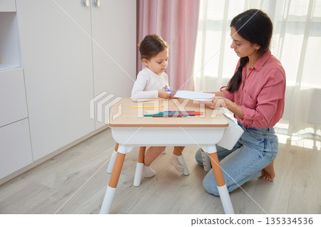 Mother and daughter cutting designs from paper with scissors for an art project 135334536