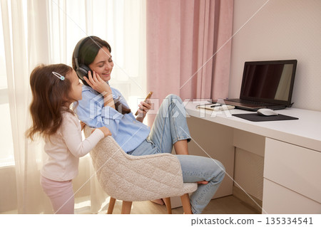 Happy mother with headphones listening to music while daughter plays 135334541
