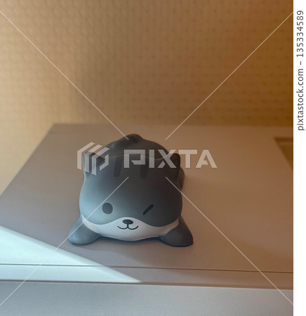 Cute gray cat figurine resting on a shelf in warm indoor light. Minimal home decor with soft shadows and cozy mood Cute gray cat figurine resting on a shelf in warm indoor light. Minimal home decor with soft shadows and cozy mood 135334589