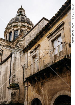Back Side Of Duomo Di San Giorgio In Ragusa, Sicily: Narrow Historic Street Leading Toward Baroque Cathedral Dome And Stone Facades 135334634