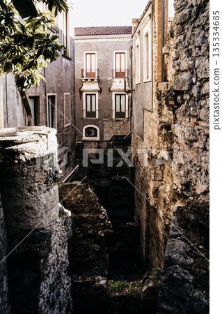Teatro Romano E Odeon In Catania, Sicily: Ancient Roman Theater Ruins With Stone Seating, Historic Buildings, And Church Towers Under Clear Daylight Teatro Romano E Odeon In Catania, Sicily: Ancient Roman Theater Ruins With Stone Seating, Historic Buildings, And Church Towers Under Clear Daylight 135334685