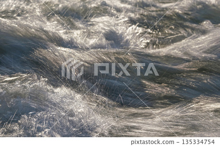 Rapid spring river flowing over rocks on sunny day, forming white water waves, longer exposure looks like threads, closeup detail - abstract nature background 135334754