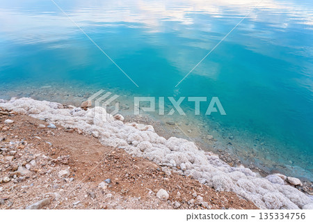 Sand covered with crystalline salt on shore of Dead Sea, turquoise blue water near - typical scenery at Ein Bokek beach, Israel Sand covered with crystalline salt on shore of Dead Sea, turquoise blue water near - typical scenery at Ein Bokek beach, Israel 135334756