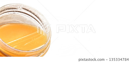 Glass jar with amber coloured honey, closeup detail, isolated on white background, space for text right side Glass jar with amber coloured honey, closeup detail, isolated on white background, space for text right side 135334784