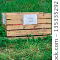 Wooden fruit crate with handwritten price sign stands on green grass in countryside. Simple rural atmosphere with natural textures 135335292