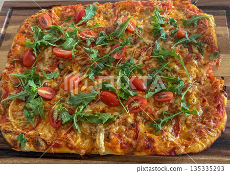 Homemade rectangular pizza topped with fresh arugula and cherry tomatoes. Golden baked crust with melted cheese creates an appetizing look 135335293