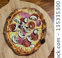 Fresh baked pizza on wooden board with melted cheese mushrooms and ham. Warm homemade food scene with natural light 135335300