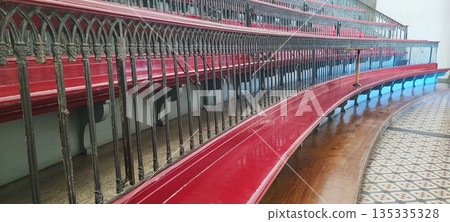 A view of empty, multi-tiered, antique wooden classroom seats with decorative railings in a historic interior. Educational system concept, timeless design. A view of empty, multi-tiered, antique wooden classroom seats with decorative railings in a historic interior. Educational system concept, timeless design. 135335328