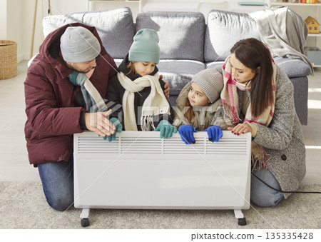Parents And Kids Keeping Warm By Electric Heater At Home 135335428