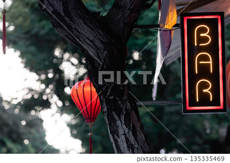 Neon sign of a bar against a backdrop of tropical greenery. Neon sign of a bar against a backdrop of tropical greenery. 135335469