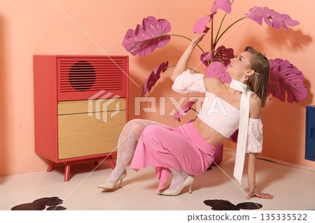 Graceful model seated with vibrant plants and vintage furniture setting Graceful model seated with vibrant plants and vintage furniture setting 135335522