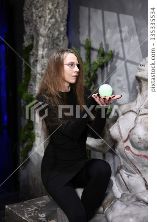 Woman with piercing gaze cradles glowing orb in abandoned city scene 135335534