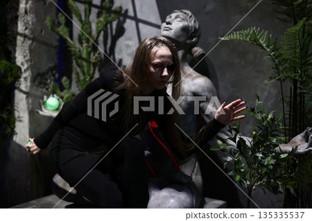 Nocturnal scene featuring woman and vinecovered statue with glowing orb Nocturnal scene featuring woman and vinecovered statue with glowing orb 135335537