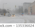 Severe snow storm hits Magdeburg city intersection cars taxi moving slowly whiteout conditions low visibility. Snow covered road traffic lights urban buildings weather disruption danger winter 135336024