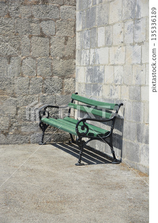 Green wooden bench by stone wall 135336189