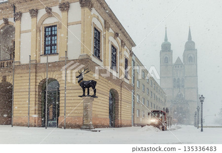 Historic Altermarkt square Magdeburg at heavy snowfall show Rathaus architecture, statues lanterns empty urban space winter storm. Municipal service tractor cleaning snow with snow plow 135336483