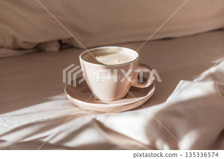 Cappuccino Cup on Cozy Bed with Sunlight and Beige Bedding Cappuccino Cup on Cozy Bed with Sunlight and Beige Bedding 135336574