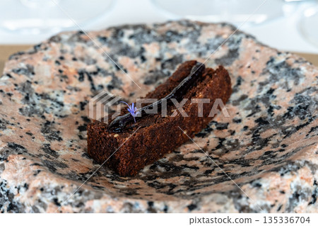 Gourmet chocolate dessert with a floral garnish served on a unique stone plate Gourmet chocolate dessert with a floral garnish served on a unique stone plate 135336704